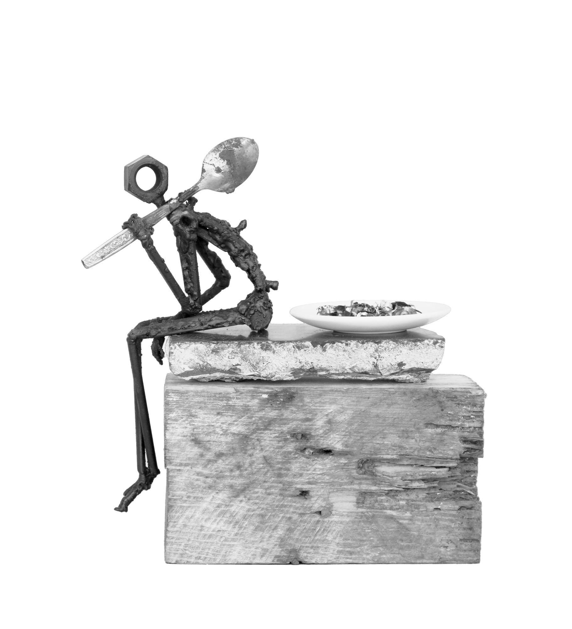 Escultura de Pedro Cuellar: figura de metal soldado sentada sobre una piedra, con una cuchara al hombro y un plato al lado