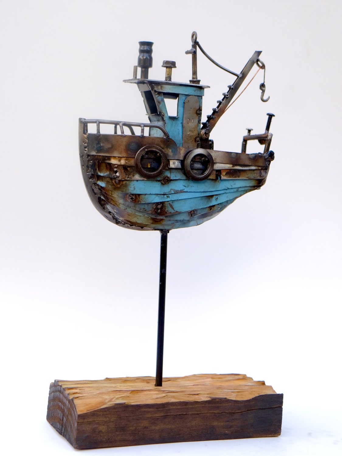 Escultura de Pedro Cuellar: barco pesquero de metal pintado de azul sobre una base de madera