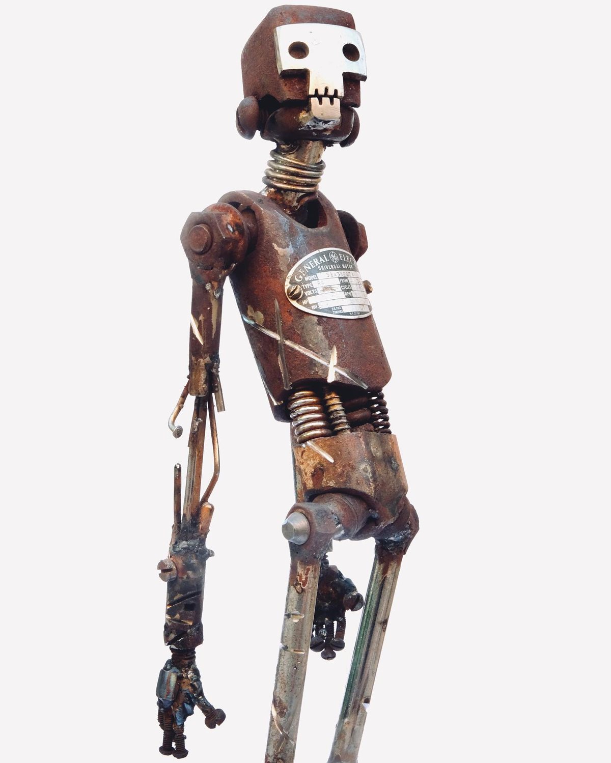 Escultura de Pedro Cuellar: robot alto de lata con resortes y una placa